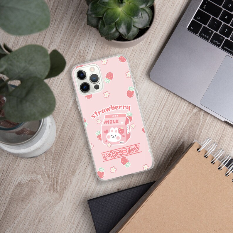 May include: A pink phone case with a cartoon strawberry milk carton and the text "strawberry" and "いちごミルク". The case is decorated with small white flowers and red strawberries.