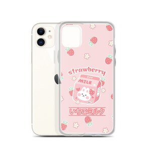 May include: A pink phone case with a clear back and a cartoon strawberry milk carton with a bunny on the front. The case is decorated with a pattern of strawberries, flowers, and the text "strawberry milk" and "いちごミルク".