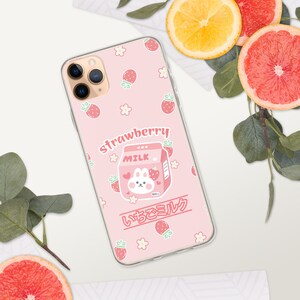 May include: A pink phone case with a cartoon strawberry milk carton and a bunny. The case has a white background with pink strawberries and white flowers. The text "strawberry" and "いちごミルク" is printed on the case.
