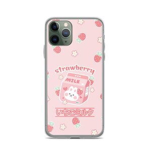 May include: A pink phone case with a cartoon strawberry milk carton and a bunny. The case has a white border and a repeating pattern of strawberries and flowers. The text "strawberry" and "いちごミルク" is printed on the case.