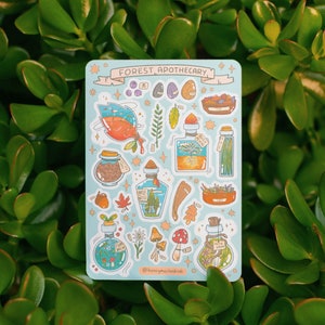 May include: A sheet of stickers with a blue background featuring illustrations of various potions, herbs, and other forest-themed elements. The text "FOREST APOTHECARY" is displayed in a banner at the top of the sheet.