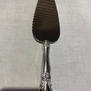 May include: A silver cake server with a serrated edge and an ornate handle. The handle has a floral design.