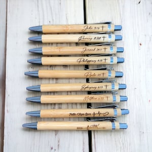 May include: A set of ten bamboo pens with blue ink and silver accents. Each pen has a different bible verse or phrase engraved on it, including "John 3:16", "Romans 8:28", "Jeremiah 29:11", "Philippians 1:13", "Psalm 23", "Ephesians 6:12", "Matthew 6:33", "Faith Hope Love", and "Faith".