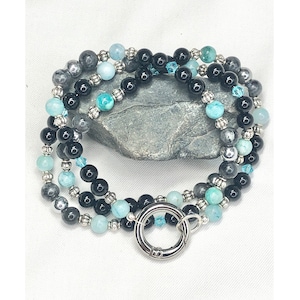May include: A triple-strand bracelet with black, grey, and blue beads. The bracelet has a silver clasp.