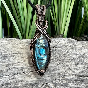 May include: A copper wire wrapped pendant featuring a blue labradorite gemstone. The pendant is hanging from a black cord.