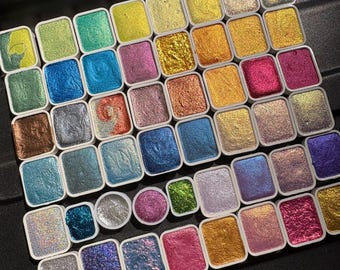 May include: A palette of 36 metallic watercolor paints in a variety of colors, including gold, silver, copper, and blue. The paints are arranged in a grid pattern and are contained in individual pans.