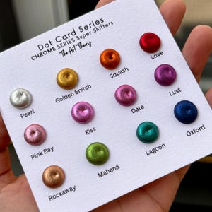 May include: A white card with the text "Dot Card Series Chrome Series Super Shifters The Art Theory" at the top. The card displays 12 small, round, metallic dots in various colors, each with a name underneath. The colors include silver, gold, orange, red, pink, green, blue, and purple.