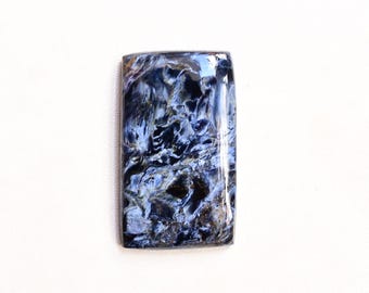 May include: Rectangular pietersite gemstone with a polished surface. The stone features a swirling pattern of dark blue, white, and black colors. The gemstone is set against a white background.