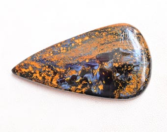 May include: A teardrop-shaped cabochon of blue tiger's eye gemstone with a golden sheen. The stone has a dark blue base with golden brown streaks and flecks.