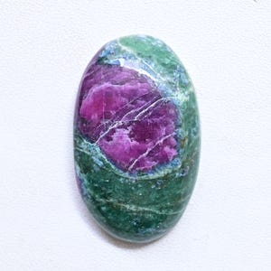 Può includere: Pietra preziosa ovale con un vivace centro magenta e un esterno screziato verde e blu. La pietra lucidata mostra venature naturali e variazioni di colore, creando un motivo unico. Ideale per la creazione di gioielli o collezionismo.