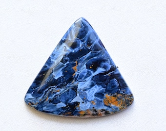 May include: A triangular-shaped gemstone with a polished surface. The stone features a swirling pattern of deep blue, light blue, and hints of orange and gold. The gemstone is set against a white background.