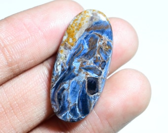 May include: A blue and gold tiger's eye cabochon gemstone with a unique pattern. The oval-shaped stone is approximately 2 inches long and 1 inch wide.