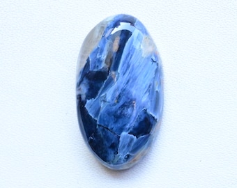 May include: Oval-shaped gemstone with a polished surface. The stone features a blend of deep and light blues, with streaks and patterns creating a unique visual texture. The gemstone is set against a white background.