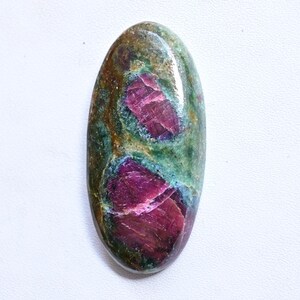 Può includere: Pietra preziosa di forma ovale con superficie lucida. La pietra presenta un mix di colori, tra cui rosso intenso, verde e marrone. Le aree rosse hanno un aspetto cristallino, mentre le sezioni verdi e marroni hanno una consistenza più screziata. La gemma è su sfondo bianco.