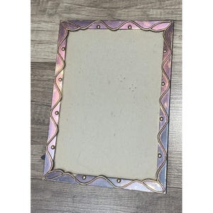 Può includere: Una cornice rettangolare con un bordo ondulato viola e oro. La cornice ha un retro grigio chiaro ed è in metallo. La cornice è vuota e pronta per visualizzare una foto.
