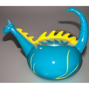 Può includere: Una teiera turchese stravagante con un design a drago. La teiera presenta un beccuccio curvo, un manico e accenti gialli sul retro e sui lati. La testa del drago forma il beccuccio e il manico si curva verso l'alto.