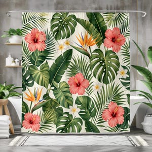 Op de afbeelding: Een douchegordijn met een tropisch bloemenpatroon. Het ontwerp bevat grote groene bladeren, roze hibiscusbloemen, witte frangipani en oranje paradijsvogelbloemen tegen een crèmekleurige achtergrond. Het gordijn hangt in een badkamer.