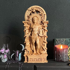 May include: A detailed wooden statue of a classical figure, possibly Apollo, holding a lyre and staff, with snakes entwined. The statue is set against a dark background, with a lit candle and other decorative items.