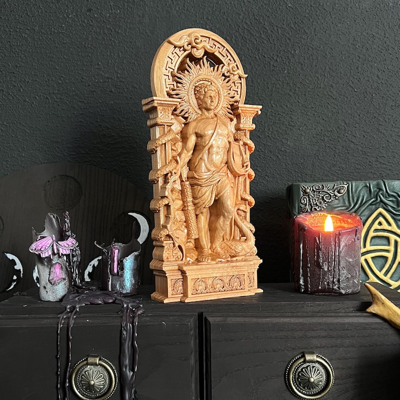 May include: A detailed wooden statue of a figure with a sunburst halo, standing within an archway. The statue is flanked by snakes and holds a club. A lit candle and other decorative items are nearby.