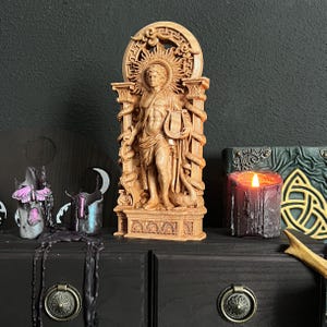 May include: A detailed wooden statue of a classical figure with a sunburst halo, holding a lyre, and flanked by snakes. The statue is on a dark wooden surface, with a lit candle and other decorative items.