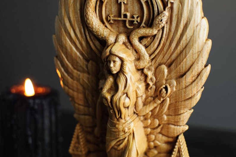 May include: A wooden carving of a woman with wings, a snake, and a symbol. The woman is wearing a crown and a long dress. The carving is painted in shades of brown and gold.