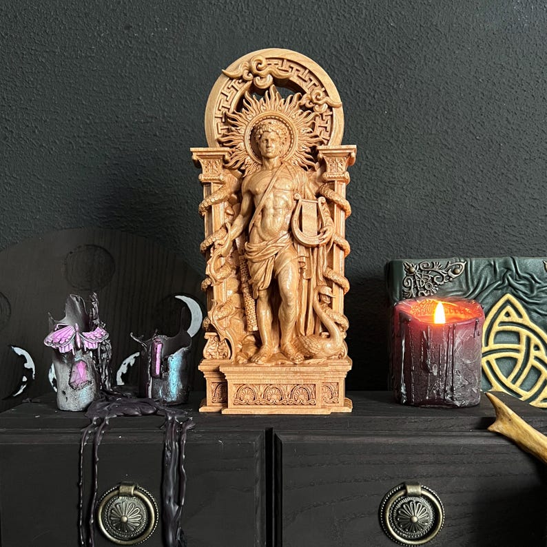 May include: A detailed wooden statue of a classical figure, possibly Apollo, holding a lyre and staff, with snakes entwined. The statue is set against a dark background, with a lit candle and other decorative items.