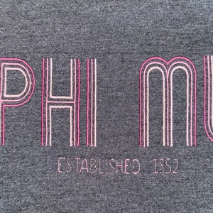 May include: A gray t-shirt with pink lettering that reads "PHI MU ESTABLISHED 1852".