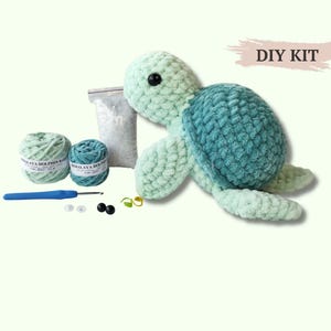 Op de afbeelding: Een DIY KIT met een gehaakte schildpad van lichtgroen en blauwgroen pluche garen. De set bevat twee bollen Himalaya Dolphin Baby garen, een blauwe haaknaald, een zakje vulling, twee zwarte veiligheidsogen en twee steekmarkeerders.