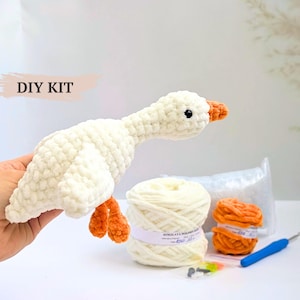 May include: A DIY kit featuring a crocheted white goose with orange feet and beak, a large skein of white yarn, a small skein of orange yarn, a blue crochet hook, a bag of stuffing, and small black safety eyes for assembly.