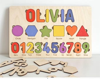 May include: Wooden puzzle board with the name "OLIVIA" in colorful letters. Features shape and number cutouts with corresponding pieces. Includes shapes like circle, hexagon, star, square, heart, and triangle. Numbers 0-9 are also included. The text "LASER READY | SVG. DXF. PDF Instant Download" is at the bottom.