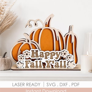 Op de afbeelding: Houten herfstdecoratie met drie pompoenen met oranje centra en een uitgesneden ontwerp. De zin "Happy Fall Y'all" wordt weergegeven in een decoratief lettertype. De basis is lichtbruin. De woorden "Laser Ready | SVG . DXF . PDF Instant Download" staan onderaan.