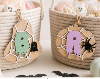 Può includere: Due cesti in corda beige con ornamenti in legno a forma di zucca appesi a spago di juta. Un ornamento mostra una lettera B verde chiaro con un piccolo fantasma, l'altro una lettera R viola chiaro con un ragno nero. Testo LASER READY SVG DXF PDF.