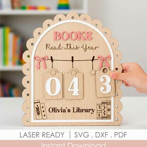 Puede incluir: Seguidor de libros de madera con el texto "BOOKS Read this Year" en rosa. Tiene tres etiquetas colgantes con los números "04" y "3". La parte inferior dice "Olivia's Library". El marco es festoneado y tiene lazos rosas.