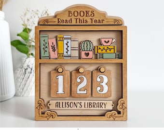May include: Wooden bookshelf-style display with the text "BOOKS Read This Year." The shelf features miniature books, a cactus, and a teacup. Below are three numbered tags and a nameplate that reads "ALLISON'S LIBRARY."
