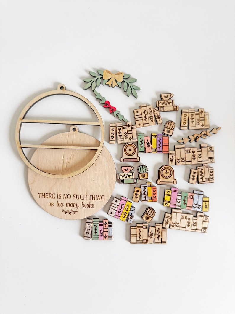 May include: Wooden bookshelf-themed ornaments and a round shelf with the text "THERE IS NO SUCH THING as too many books." The ornaments include miniature books, clocks, and a wreath with a bow. The color palette includes natural wood, green, pink, yellow, and blue.