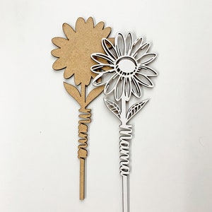 May include: Two wooden flower cutouts, one brown and one white. The white flower has the word "Mama" written on the stem.