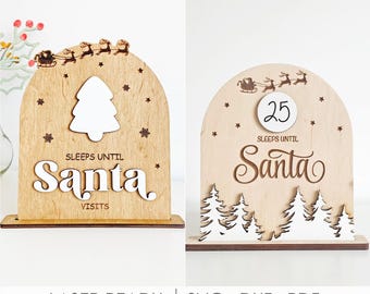 Puede incluir: Dos letreros de madera arqueados con diseños cortados con láser de Santa en un trineo con renos. Los letreros muestran el texto "SLEEPS UNTIL Santa VISITS" y "SLEEPS UNTIL Santa" con un inserto circular de números, estrellas y pinos.