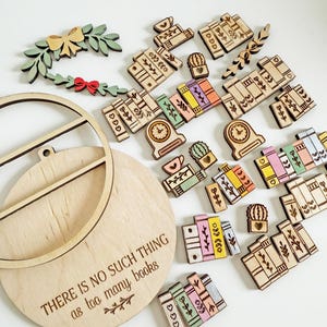 May include: A collection of wooden book-themed embellishments, including miniature books, clocks, cacti, and a wreath with a bow. A wooden plaque with the text "THERE IS NO SUCH THING as too many books" is also present. The items are in various colors.