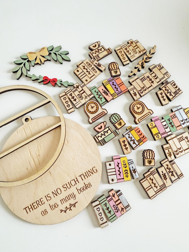 May include: A collection of wooden book-themed embellishments, including miniature books, clocks, cacti, and a wreath with a bow. A wooden plaque with the text "THERE IS NO SUCH THING as too many books" is also present. The items are in various colors.