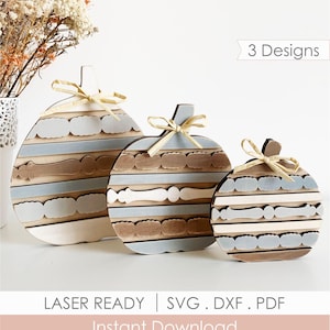 May include: Three flat wooden pumpkin cutouts in descending sizes, each featuring horizontal stripes in white, light blue, and natural wood tones. Each pumpkin is topped with a small, tied raffia bow. Text on image reads 3 Designs, LASER READY, SVG . DXF . PDF, Instant Download.