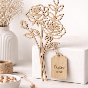 Puede incluir: Ramo de rosas de madera cortado con l&aacute;ser con una etiqueta que dice "Rose June". El ramo presenta dos rosas abiertas, capullos y hojas. La etiqueta est&aacute; sujeta con hilo. El color general es marr&oacute;n claro.