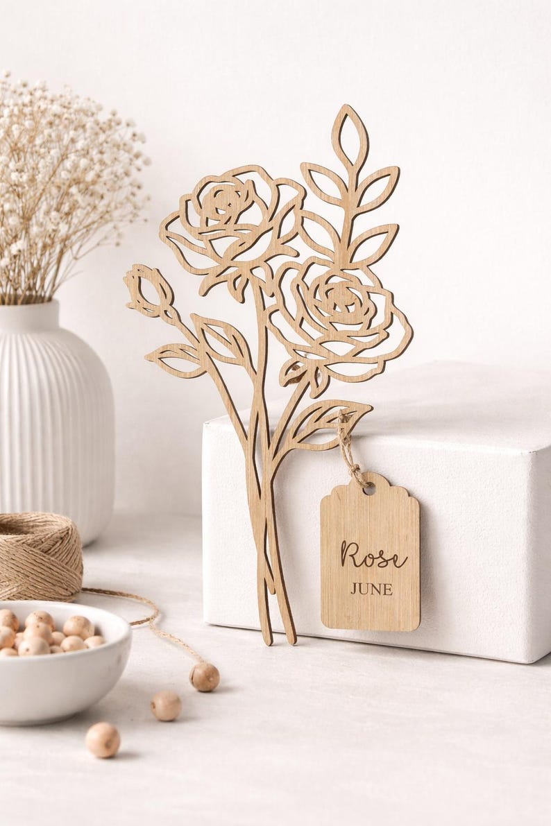Puede incluir: Ramo de rosas de madera cortado con l&aacute;ser con una etiqueta que dice "Rose June". El ramo presenta dos rosas abiertas, capullos y hojas. La etiqueta est&aacute; sujeta con hilo. El color general es marr&oacute;n claro.