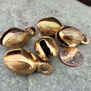 May include: Five gold-coloured metal bells with a leaf design. The bells are approximately the size of a UK 20 pence coin.