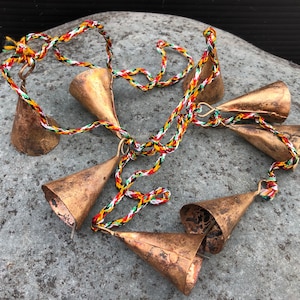 May include: A string of six small, copper-colored bells with a colorful, braided cord. The bells are tied together with a knot at the top of each bell.