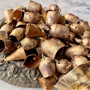 May include: A collection of antique gold-toned bells with a distressed finish. The bells are arranged in a pile on a decorative surface.