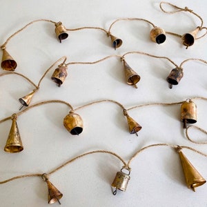 May include: A string of gold-toned bells hanging from a natural twine rope. The bells are various shapes and sizes, and some have a slightly distressed finish.