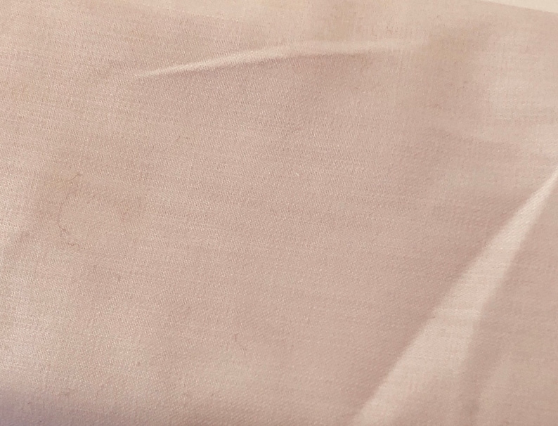 May include: A close-up shot of a light pink fabric with a subtle texture. The fabric has soft folds and creases, creating shadows and highlights. The overall appearance is smooth and delicate, with a muted color palette.