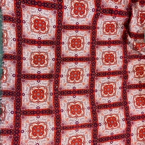 K&ouml;nnte beinhalten: Roter und wei&szlig;er Stoff mit einem sich wiederholenden Muster aus komplizierten quadratischen Designs. Der Stoff hat ein paisleyartiges Design mit einem burgunderfarbenen Hintergrund.