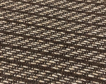 May include: Close-up of a brown fabric with a white woven pattern. The fabric has a textured, slightly rough surface.
