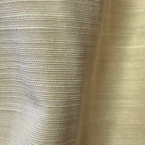 Könnte beinhalten: Nahaufnahme eines beigefarbenen Stoffes mit gewebter Struktur. Der Stoff hat einen dezenten Glanz und eine leicht strukturierte Oberfläche.